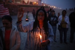 FILE - A woman holding a candle observes a minute of silence in memory of migrants who have died during their journey toward the U.S., near the border fence that separates Mexico from the U.S., in Tijuana, Mexico, June 29, 2019.