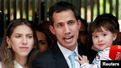 Venezuelan opposition leader and self-proclaimed interim president Juan Guaido talks to media next to his wife Fabiana Rosales, while carrying their daughter outside their home in Caracas, Jan. 31, 2019.