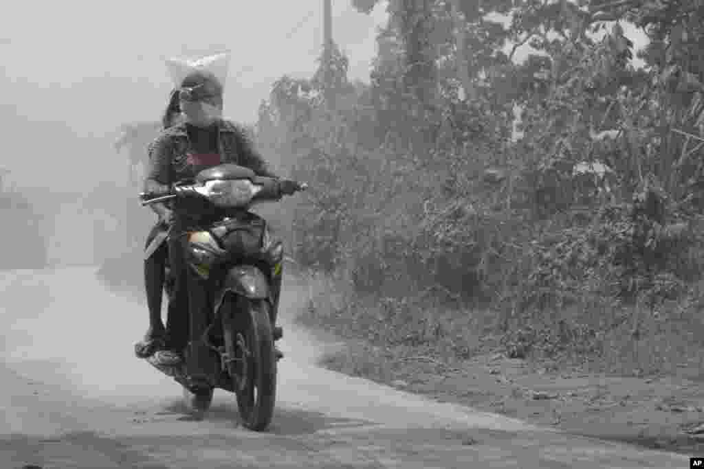 Villagers ride a motorcycle on a road covered with volcanic ash from the eruption of Mount Sinabung in Kuta Mbaru, North Sumatra, Indonesia, Nov 18, 2013.