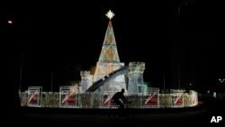 FILE - A man rides a bicycle past Christmas decorations on a street in Lagos, Dec. 20, 2024.