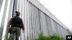 FILE - A policeman patrols alongside a steel wall at Evros River, near the village of Poros, at the Greek -Turkish border, Greece, May 21, 2021.