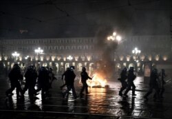 Police officers are seen in front of a garbage bin set on fire during a protest against new government restrictions to curb the spread of the coronavirus, in Turin, Italy, Oct. 26, 2020.