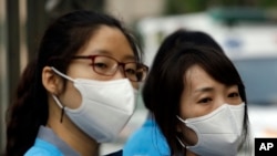 South Korean health workers wearing masks as a precaution against MERS, Middle East Respiratory Syndrome, virus, wait to check examinees' temperature and to sanitize their hands at a test site for a civil service examination in Seoul, South Korea, Saturday, June 13, 2015.