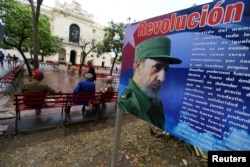 People sit in front of a billboard with a message about Cuba's late President Fidel Castro in Santa Clara, Cuba, Nov. 30, 2016.