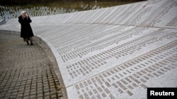 FILE - A woman walks past memorial plaques at the Potocari Genocide Memorial Center near Srebrenica, March 18, 2015.
