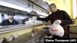 In this Tuesday, March 31, 2020, photo,In this Tuesday, March 31, 2020, photo, Glen Quadros, right, owner of the Great American Diner & Bar, checks a takeout order as cook Arturo Aguilar looks on in Seattle. (AP Photo/Elaine Thompson)