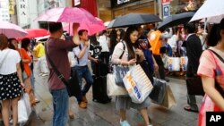 Khách du lịch Trung Quốc chờ xe buýt tham quan ở phía trước của một cửa hàng điện tử giảm giá ở quận Ginza, Tokyo.