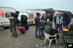 Migrants carrying their belongings walk past other migrants warming themselves around a fire as they leave a makeshift camp known as "the jungle" near Calais, northern France, to register at a processing center, Oct. 24, 2016.