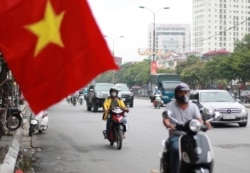 FILE - People wearing face masks to help curb the spread of the coronavirus ride mopeds in Hanoi, Vietnam on Thursday, Aug. 6, 2020.