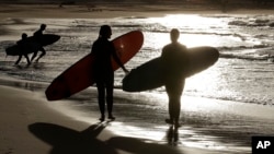 In this April 28, 2020, file photo, surfers walk along Bondi Beach in Sydney as coranavirus pandemic restrictions are eased. U.S. biotechnology company Novavax began injecting a coronavirus vaccine candidate into people in Australia.