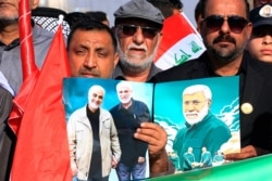 FILE - Supporters of the PMF hold a poster of Abu Mahdi al-Muhandis, deputy commander of Popular Mobilization Forces, and General Qassem Soleimani, head of Iran's Quds force, during a rally to commemorate their deaths, in Basra, Iraq, Jan. 8, 2021.