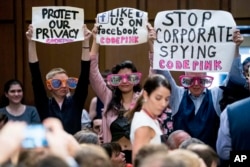 Members of the audience hold up signs and wear sunglasses that read "Stop Spying" before CEO Mark Zuckerberg arrives to testify before a joint hearing of two Senate committees on Capitol Hill in Washington, April 10, 2018, about the use of Facebook data t