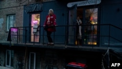 Жена стои на балкон над електричен генератор во Киев, Украина, на 28 ноември 2024 година, по руските напади врз украинската енергетска инфраструктура