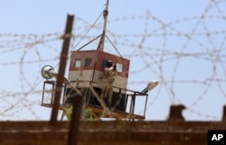 FILE - An Egyptian soldier on a watchtower looks through binoculars as bulldozers work on creating a buffer zone along the Egyptian border with the Gaza strip, in Rafah, June 28, 2017.