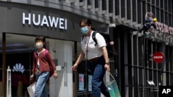 Residents wearing face masks to protect against the coronavirus walk past a Huawei retail store in Beijing, May 18, 2020.