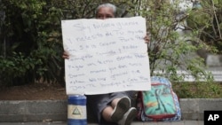 FILE - A Nicaraguan exile, who wishes to only be identified by her nickname "La Profe," Spanish for "the teacher," holds a sign asking for spare change in Alajuela, Costa Rica, March 29, 2019. 