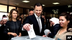 Syrian President Bashar al-Assad casts his ballot in parliamentary elections as wife Alma, left, observes, in Damascus, April 13, 2016. The photo was posted on the official Facebook page of the Syrian Presidency. 