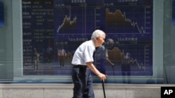 FILE - An elderly man walks by an electronic stock board of a securities firm in Tokyo, Aug. 19, 2016. The elderly are said to be more prone to depression as they became more isolated from their communities.