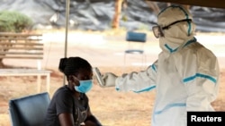 FILE - A woman has her temperature checked by a health care worker during a nationwide lockdown to help curb the spread of the coronavirus, at a screening center in Harare, Zimbabwe, April 30, 2020.