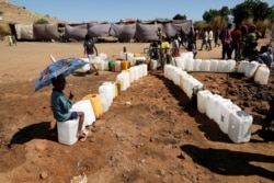 FILE - An Ethiopian refugee child holds an umbrella while sitting in line for water, at the Um Rakouba refugee camp on the Sudan-Ethiopia border in Sudan, Nov. 29, 2020.