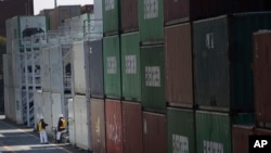FILE - Port workers chat next to a pile of cargo at a container terminal in Tokyo, Feb. 19, 2015. Japan has recorded a trade surplus for September of 139.6 billion yen ($1.2 billion), but exports fell 1.2 percent from the previous year, marking the first decline since 2016, after several natural disasters.