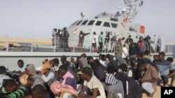 Rescued migrants are seated next to a coast guard boat in the city of Khoms, around 120 kilometers (75 miles) east of Tripoli, Libya, Oct. 1, 2019. 