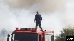 A firefighter looks at smoke from the roof of a fire vehicle after a wildfire broke out in Kitsi, a southern suburb of Athens on June 19, 2024.