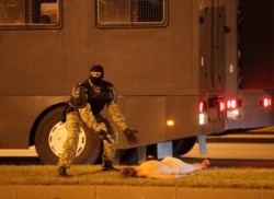 A law enforcement officer gestures next to an injured protester Yevgeny Zaichkin during clashes after presidential election polls closed in Minsk, Belarus, Aug. 9, 2020.