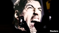 People use mobile devices to take pictures of an advertising placard showing Uruguay's striker Luis Suarez flashing his teeth, Copacabana beach, Rio de Janeiro, June 26, 2014.
