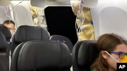 This image provided by Kelly Bartlett shows passengers near a hole in the fuselage of an Alaska Airlines Boeing 737 Max 9, Flight 1282, which was forced to return to Portland International Airport on Jan. 5, 2024. 