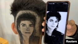 Gurwinder Singh Sidhu, 31, a barber, displays a photo of Michael Jackson next to a customer after he made a hair tattoo of the pop star in the customer's hair inside his shop. (REUTERS/Sunil Kataria)
