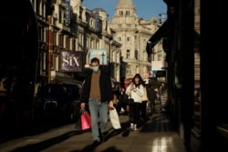 A man walks with shopping bags along Shaftesbury Avenue, in London, backdropped by theatres that have had to temporarily close as the British government have moved London into coronavirus Tier 3 restrictions, Dec. 17, 2020.