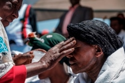 A woman draws a cross with oil on the forehead of another woman during a memorial ceremony at the crash site of the Ethiopian Airlines Flight 302 airplane accident in Tulu Fara, Ethiopia, on March 8, 2020.