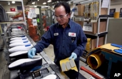 FILE - Khan Simom of Boston glues cushions to unfinished shoes during the assembly process at the New Balance Athletic Shoe, Inc. factory in Boston, May 1, 2012.
