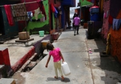 A girl walks carrying drinking water at a slum in Mumbai, India, Wednesday, June 19, 2019.