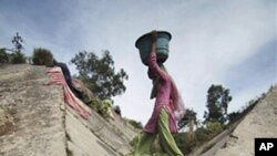 An Indian girl crosses over a stream of polluted water as she carries drinking water on the outskirts of Jammu, India, March 21, 2011