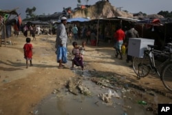 FILE - A Rohingya Muslim girl carries her baby sister as she walks across a stream of drainage water at the Thaingkhali refugee camp on Nov. 22, 2017.