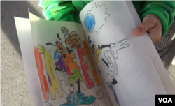 Alex shows his coloring book that someone in Mexico donated to him. The eight-year-old a migrant child from Honduras was waiting at the El Paso del Norte Bridge between Mexico and the U.S. with his father for a chance to request asylum. (VOA video screengrab)