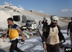 FILE - Syrian civil defense members search near a burned vehicle and personal belongings at a site in Hass town after an airstrike in the southern part of Syria's Idlib province, Sept. 8, 2018.