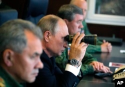 Russian President Vladimir Putin, center, Defense Minister Sergei Shoigu, left, and Chief of the General Staff of the Russian Armed Forces Valery Gerasimov, right, watch a military exercise at a training ground at the Luzhsky Range.