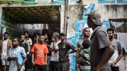 Vijana wanawatizama polisi wa kupambana na ghasia wakipiga doria mtaa wa Stone Town Zanzibar