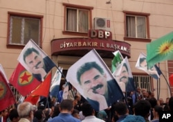 FILE - People hold posters of jailed PKK leader Abdullah Ocalan and PKK flags as they gather outside the headquarters of pro-Kurdish Democratic Regions Party, DBP, on the17th anniversary of Ocalan’s expulsion from Syria, in Diyarbakir, Turkey, Oct. 9, 2015.