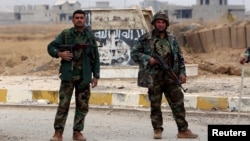 FILE - Kurdish Peshmerga fighters stand in a street against the backdrop of a defaced Islamic State flag in the town of Sinjar, northern Iraq, Nov. 16, 2015.