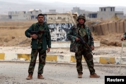 FILE - Kurdish Peshmerga fighters stand in a street against the backdrop of a defaced Islamic State flag in the town of Sinjar, northern Iraq, Nov. 16, 2015.