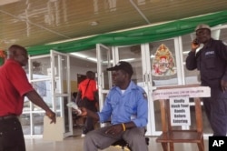 FILE - A health worker takes a man's temperature, center, before his is allowed to enter into a government building, with a message, right, reading "Kindly wash your hands before entering" the building in Monrovia, Liberia, Jan. 14, 2016.