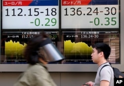 People walk by an electronic board displays exchange rate of euro, left, and British pound at the securities firm in Tokyo, June 27, 2016.