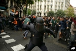 In this Oct. 1, 2017 photo, a Spanish riot police swings a club against would-be voters near a school assigned to be a polling station by the Catalan government in Barcelona, Spain.