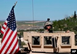 FILE - In this April 4, 2018, photo, a U.S. soldier sits on his armored vehicle on a road leading to the tense front line in Manbij, Syria.
