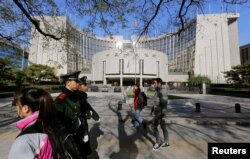 People walk past the headquarters of the People's Bank of China as two police officials patrol the area in Beijing Nov. 20, 2013.