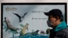 FILE - A man wearing a protective face mask walks by a government poster promoting the protection of wildlife animals following the coronavirus outbreak, in Beijing, China, March 11, 2020. The poster is viewed by critics as propagandistic in nature.